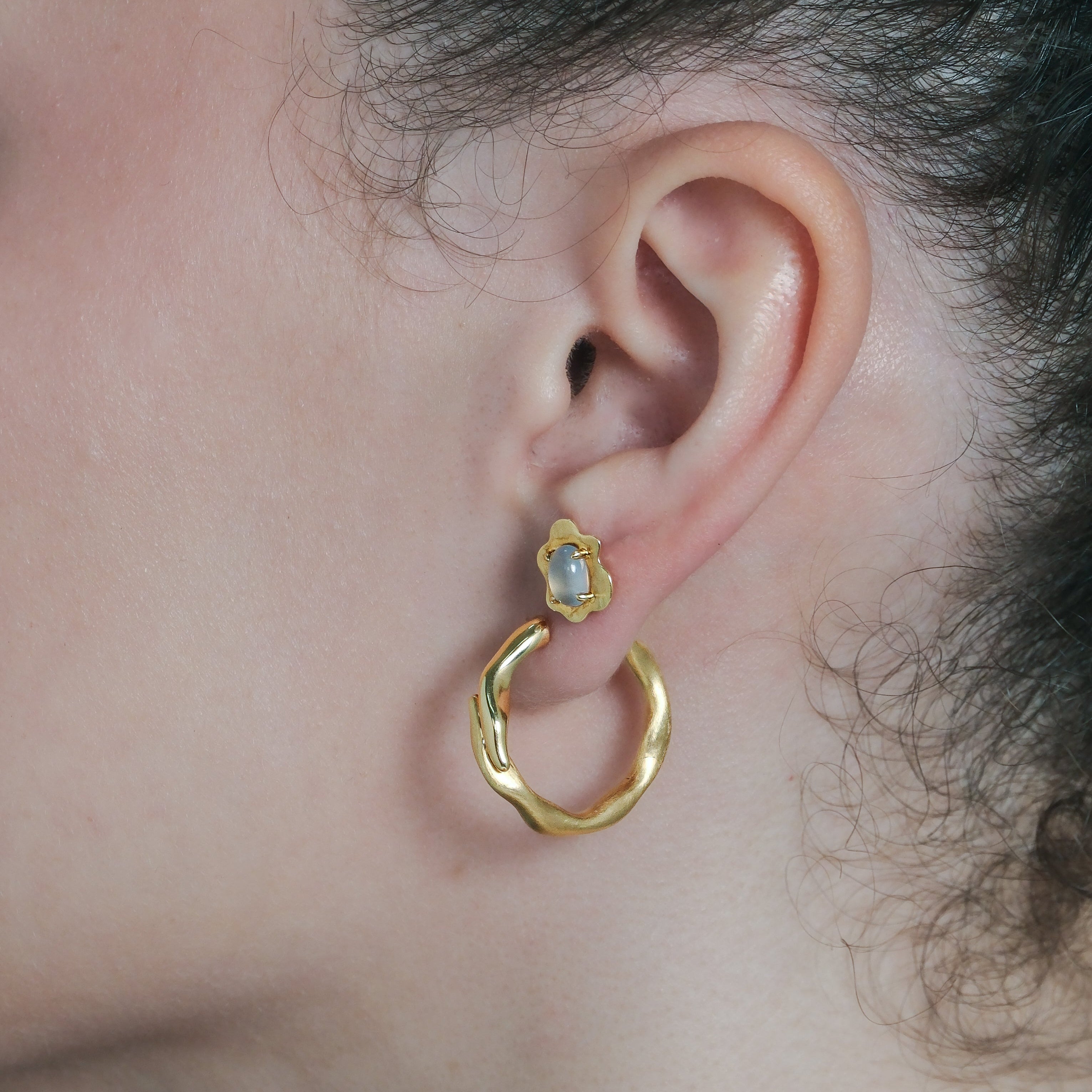 Close-up of a person wearing gold hoop earrings with a small stud with gemstone.