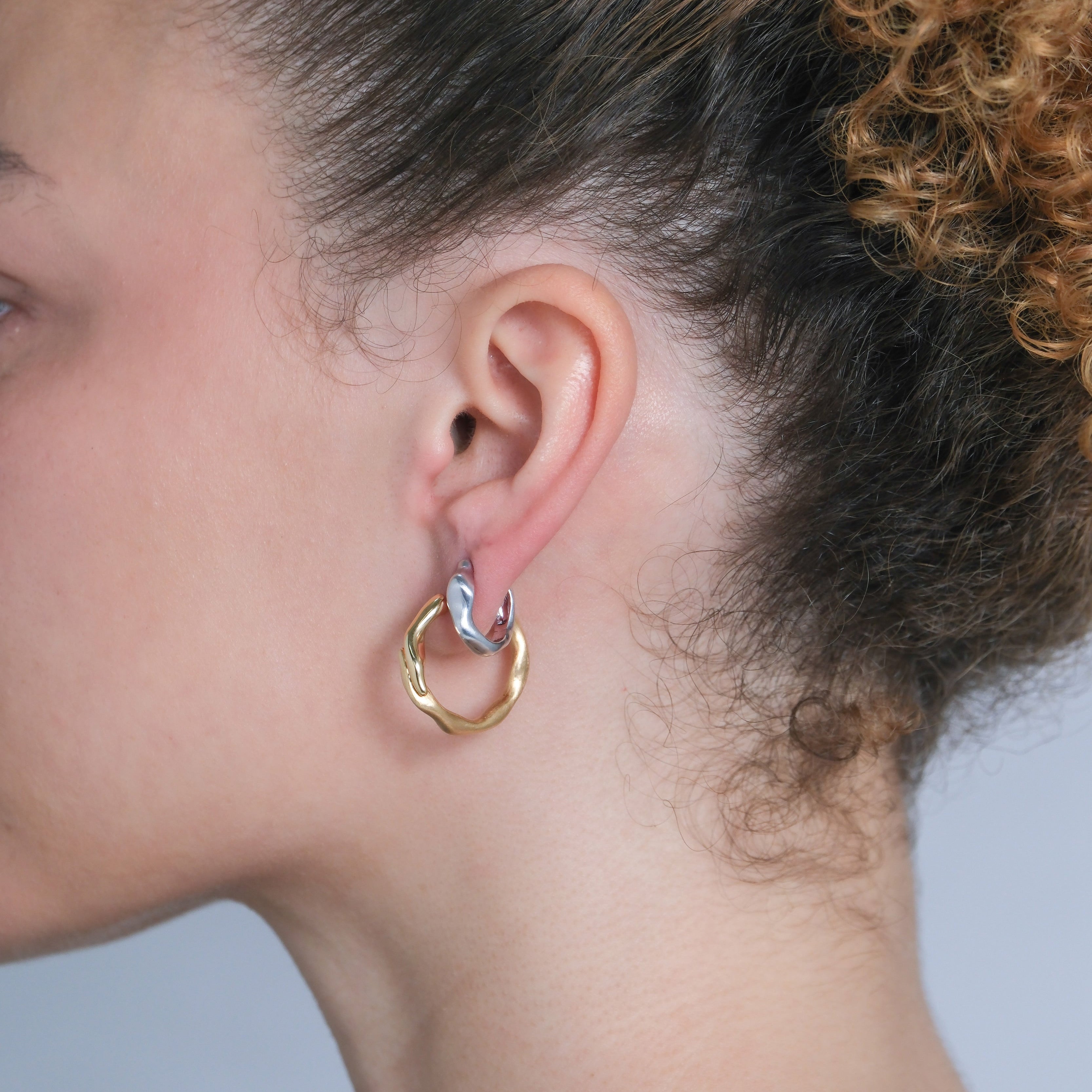 Close-up of a person wearing a gold hoop earring and a silver hoop earring on a neutral background