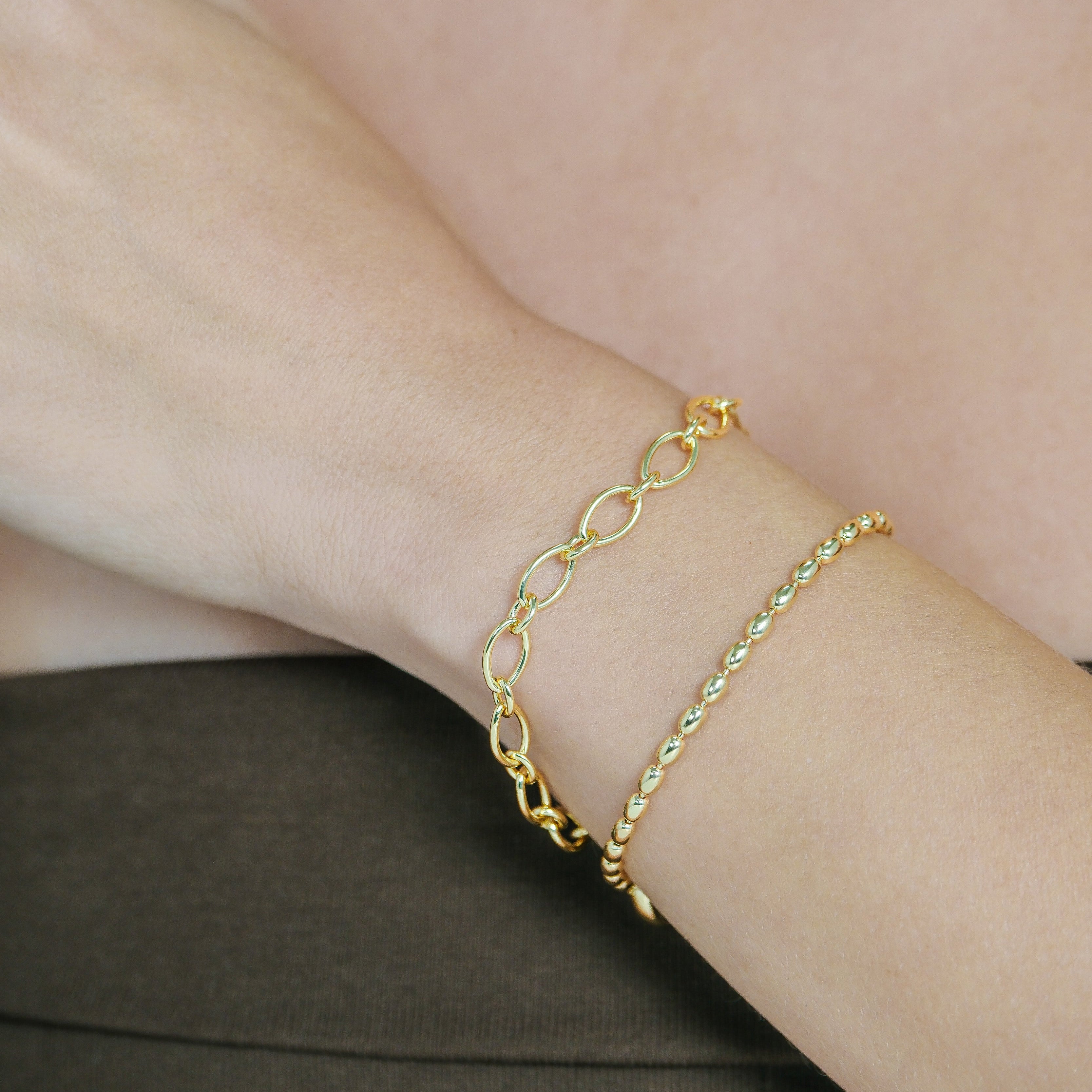Gold chain bracelet on a person's wrist with a neutral background