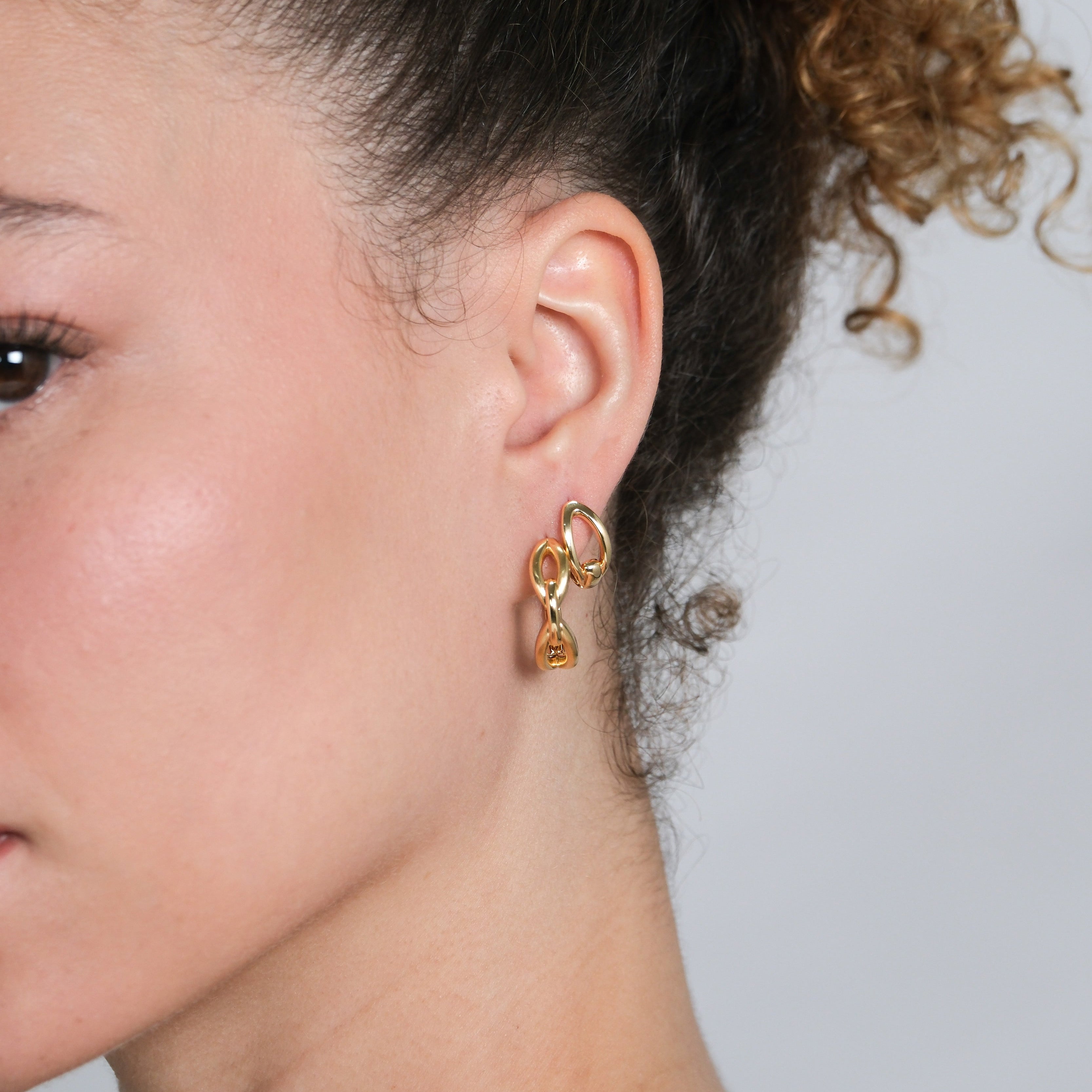 Close-up of a person wearing a gold earring with a small pendant on a neutral background