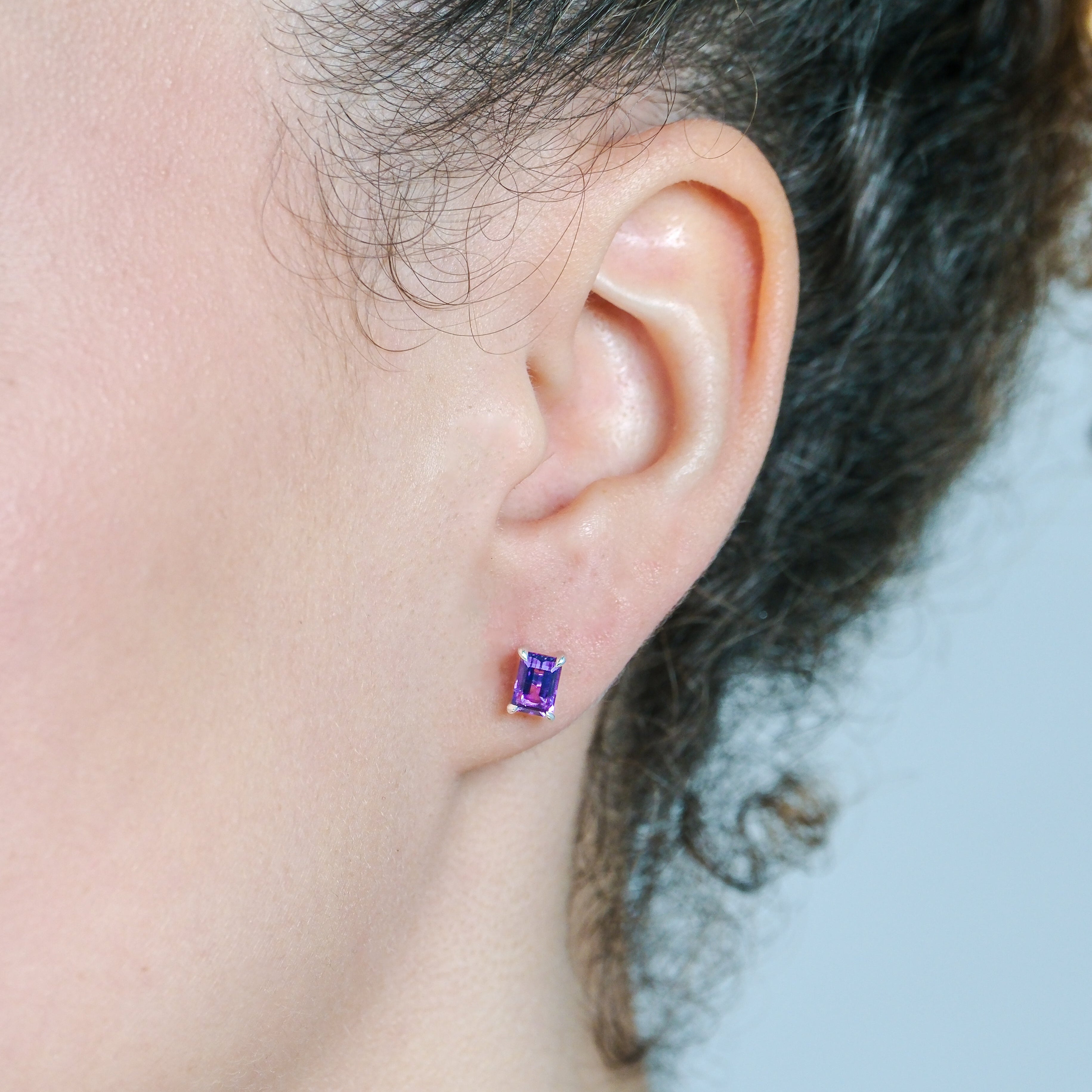 Close-up of an ear wearing a small purple earring with a blurred background