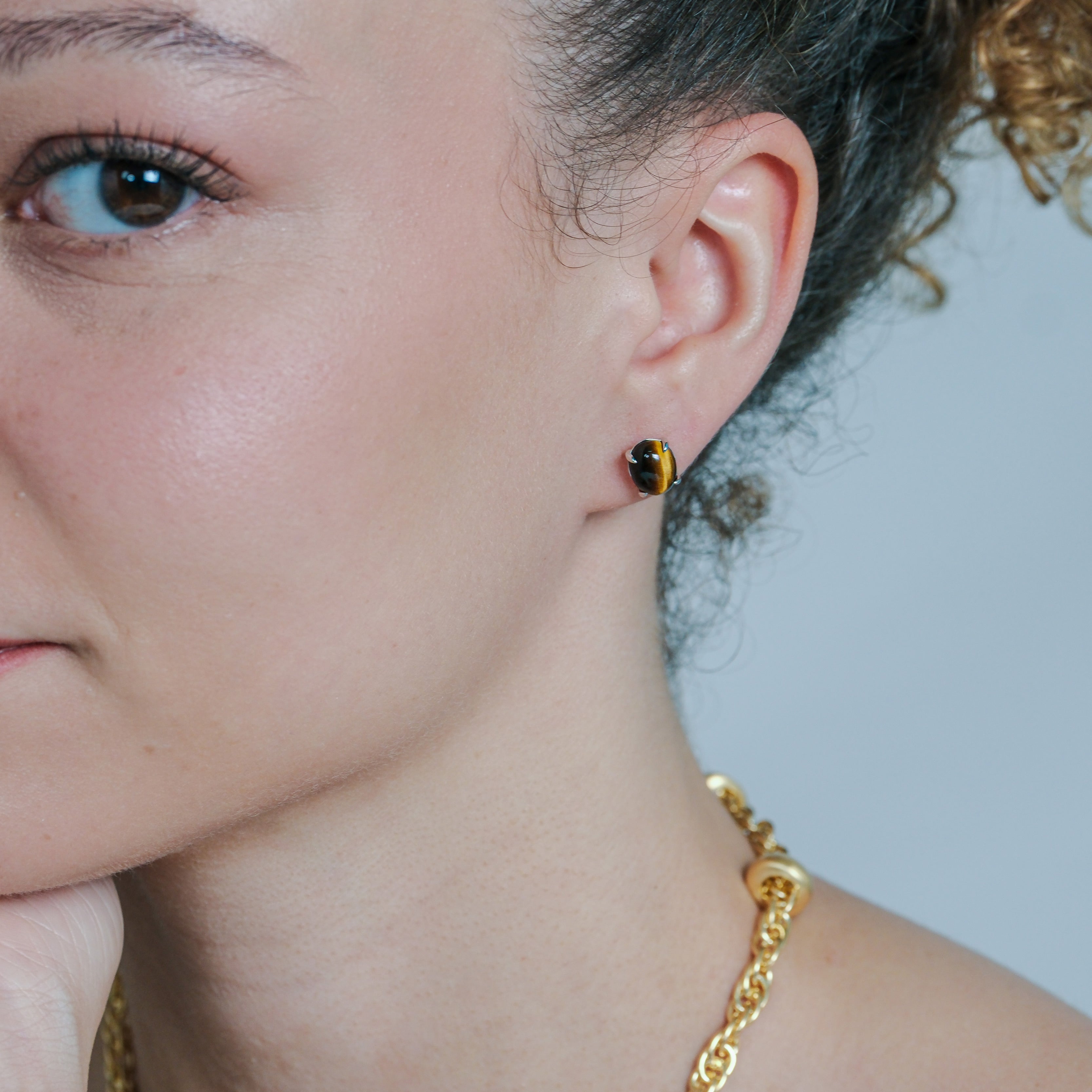 Close-up of a person wearing a gold chain necklace and a small black and brown earring.