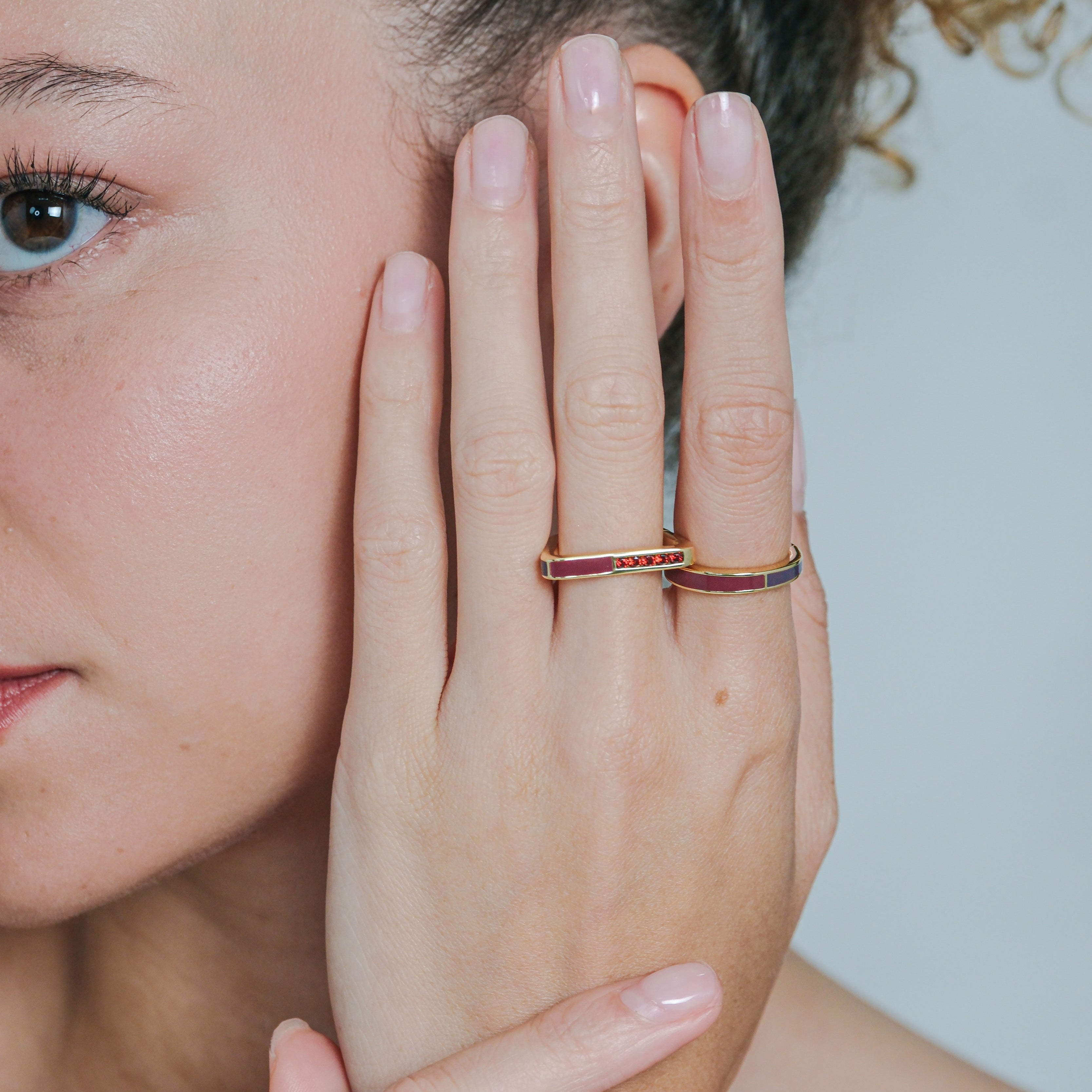 Close-up of a woman's hand with a ring on her finger, touching her face.