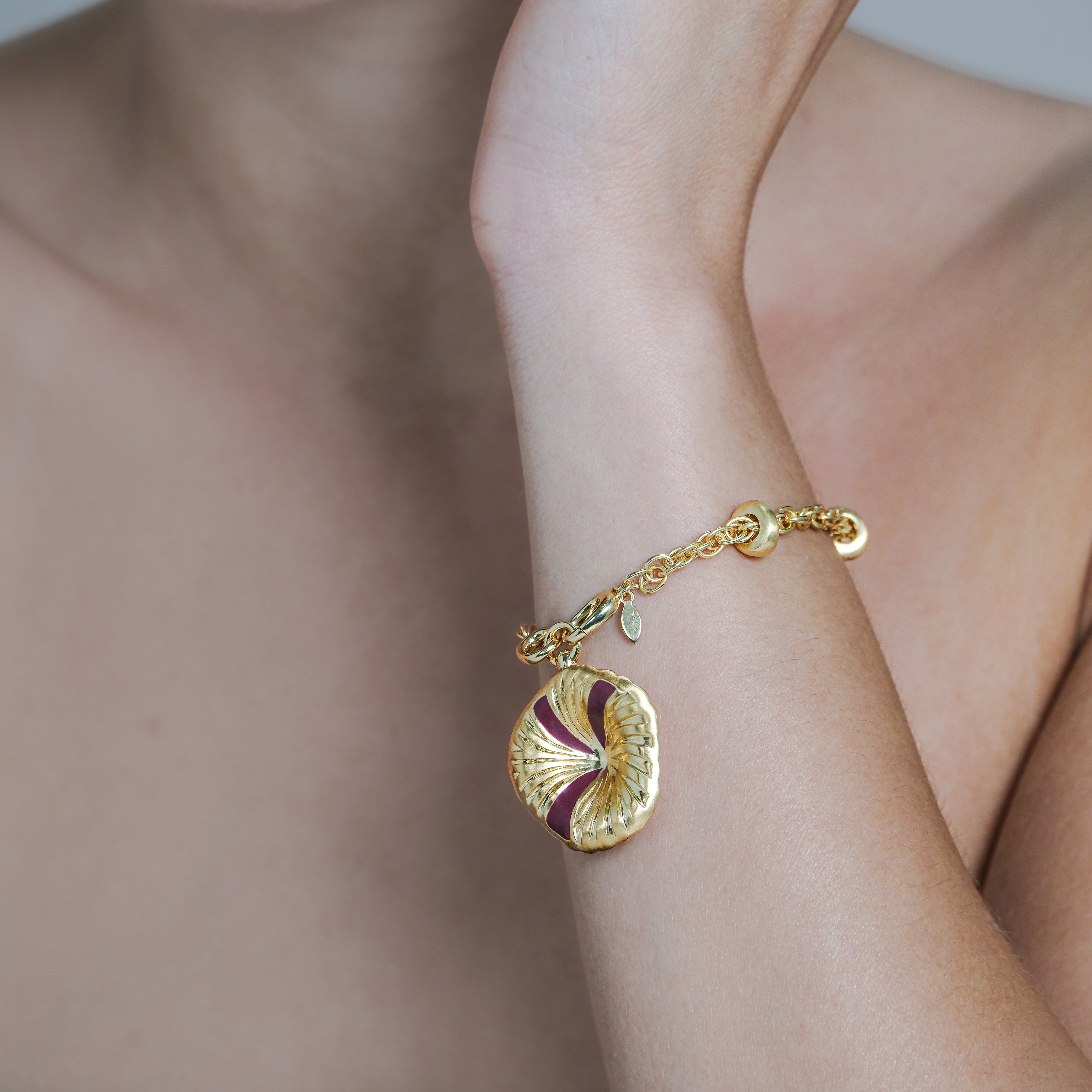 Gold bracelet with a charm on a person's wrist against a neutral background