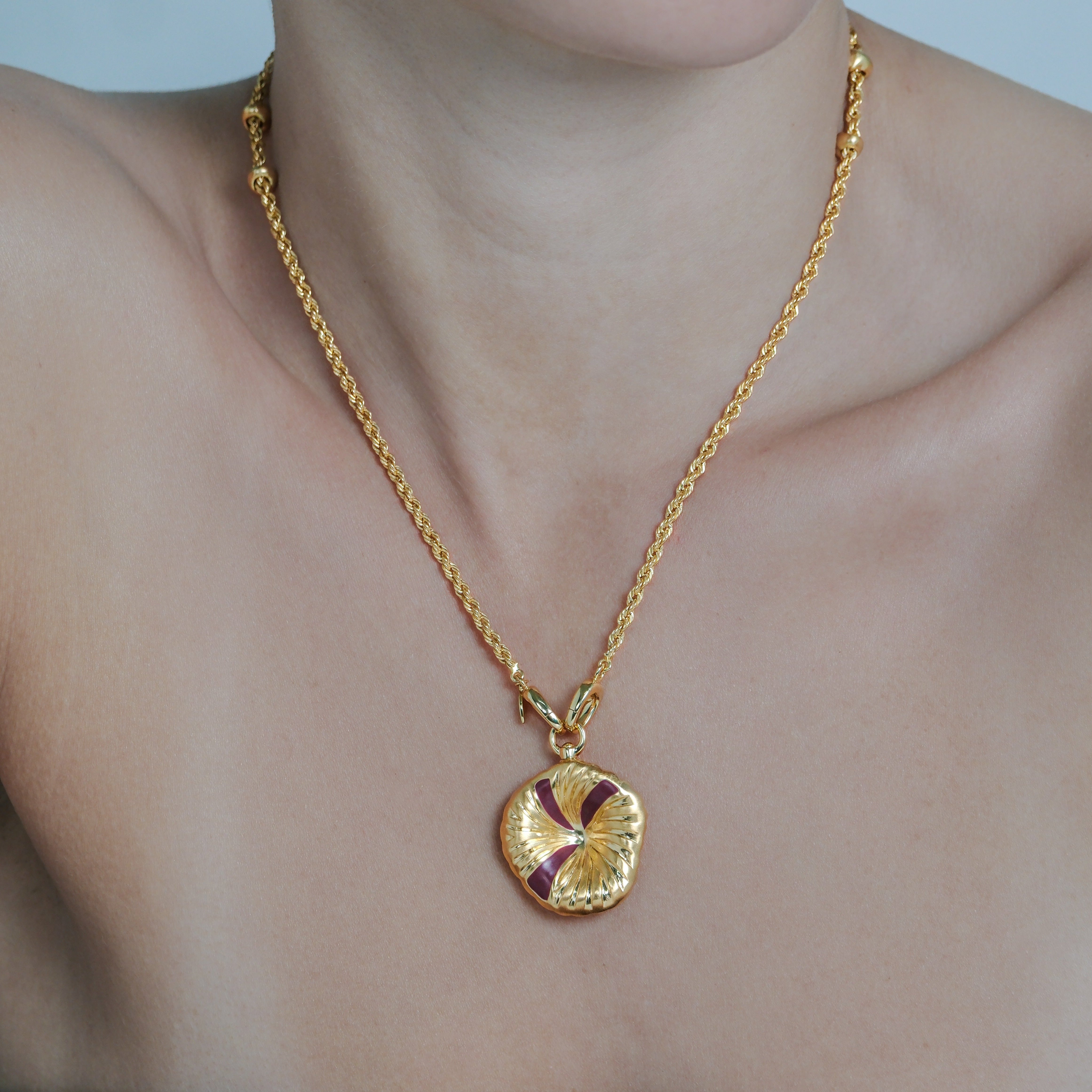 Gold necklace with a circular pendant on a person's neck against a neutral background