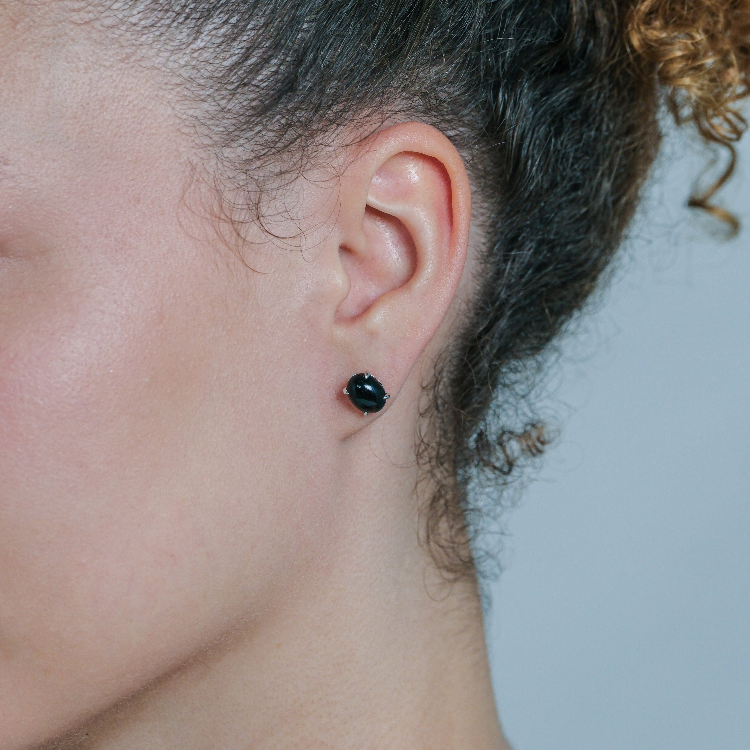 Close-up of a person wearing a black earring on a neutral background