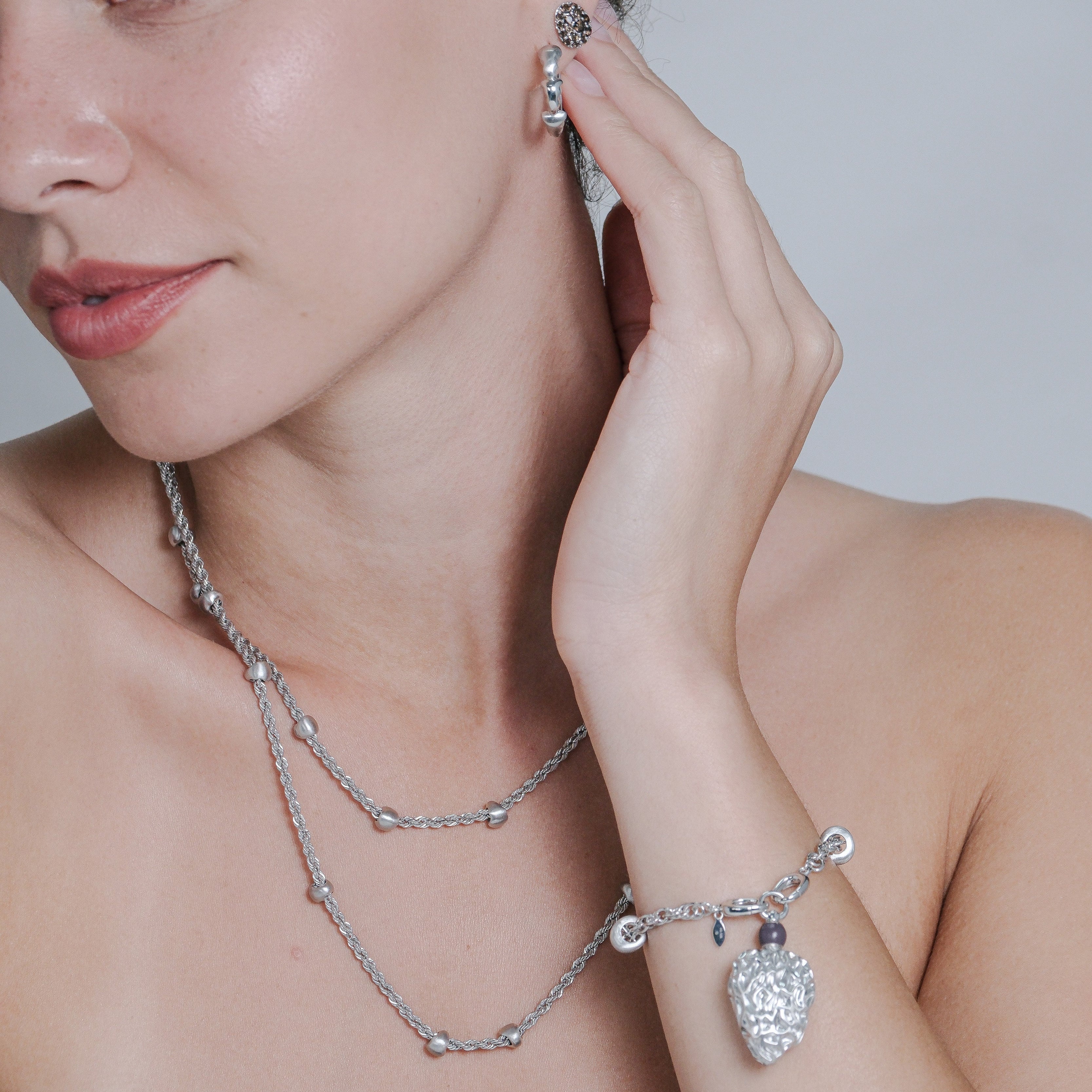 Woman wearing silver jewelry including a necklace, bracelet, and earrings on a plain background