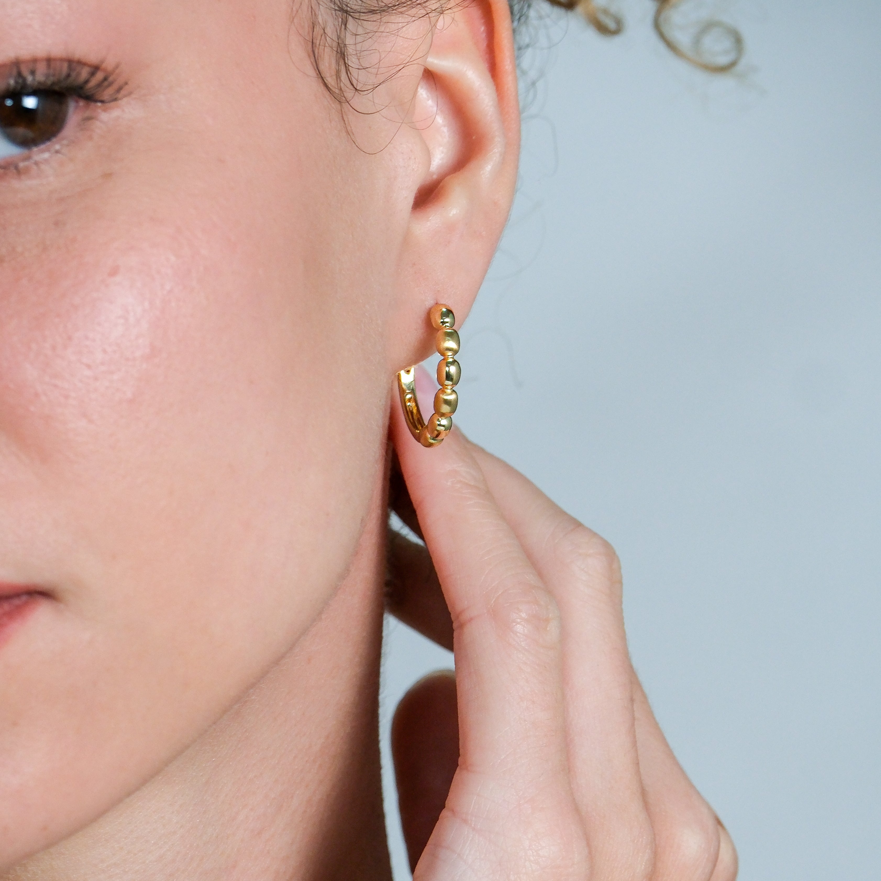 Close-up of a gold hoop earring worn by a person with a neutral background