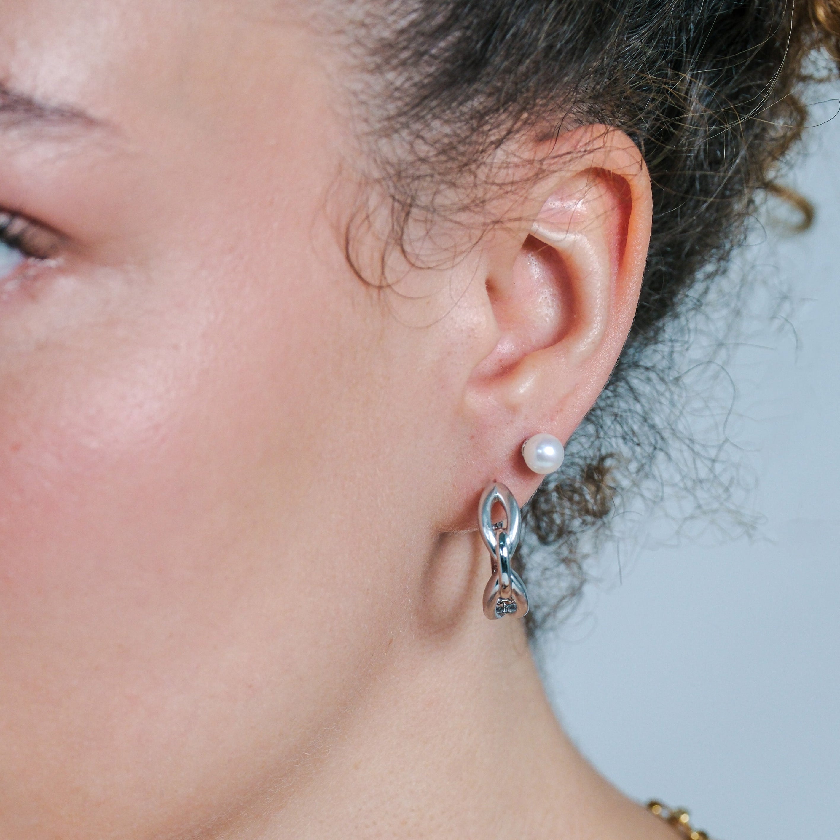 Close-up of a woman wearing a gold necklace and silver hoop earrings with a pearl accent.