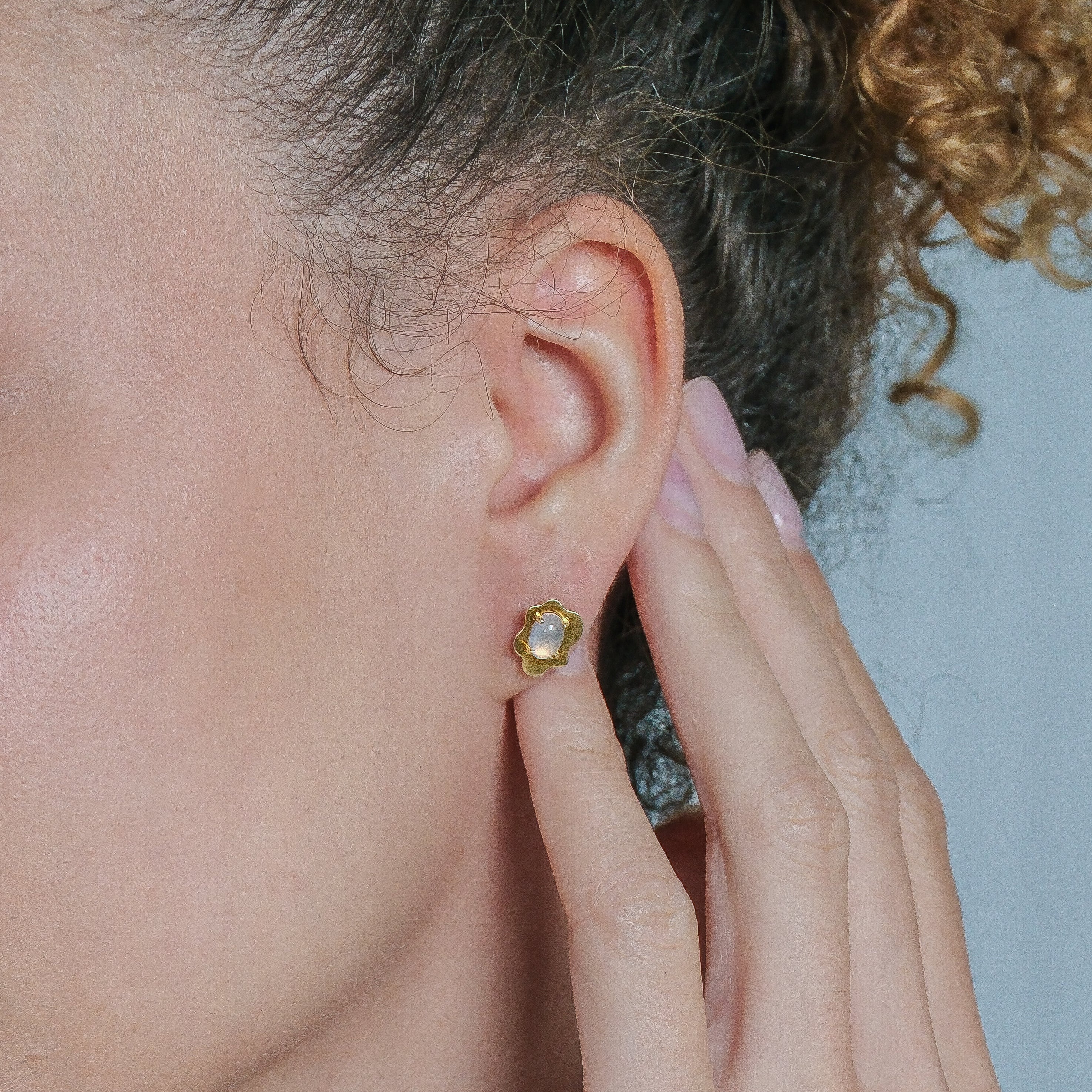 Close-up of a person wearing a gold earring with a clear gemstone.