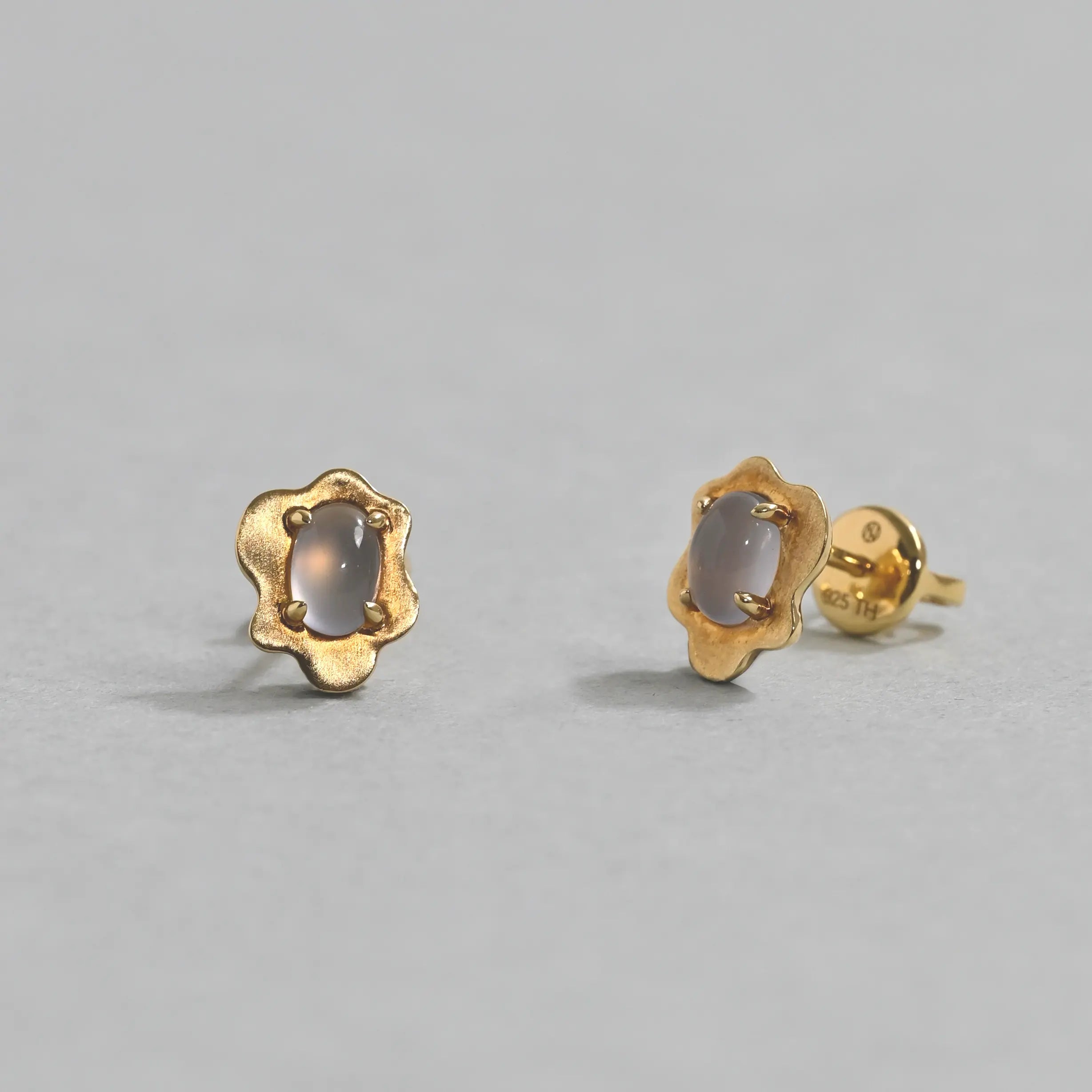Gold earrings with a central gemstone on a gray background