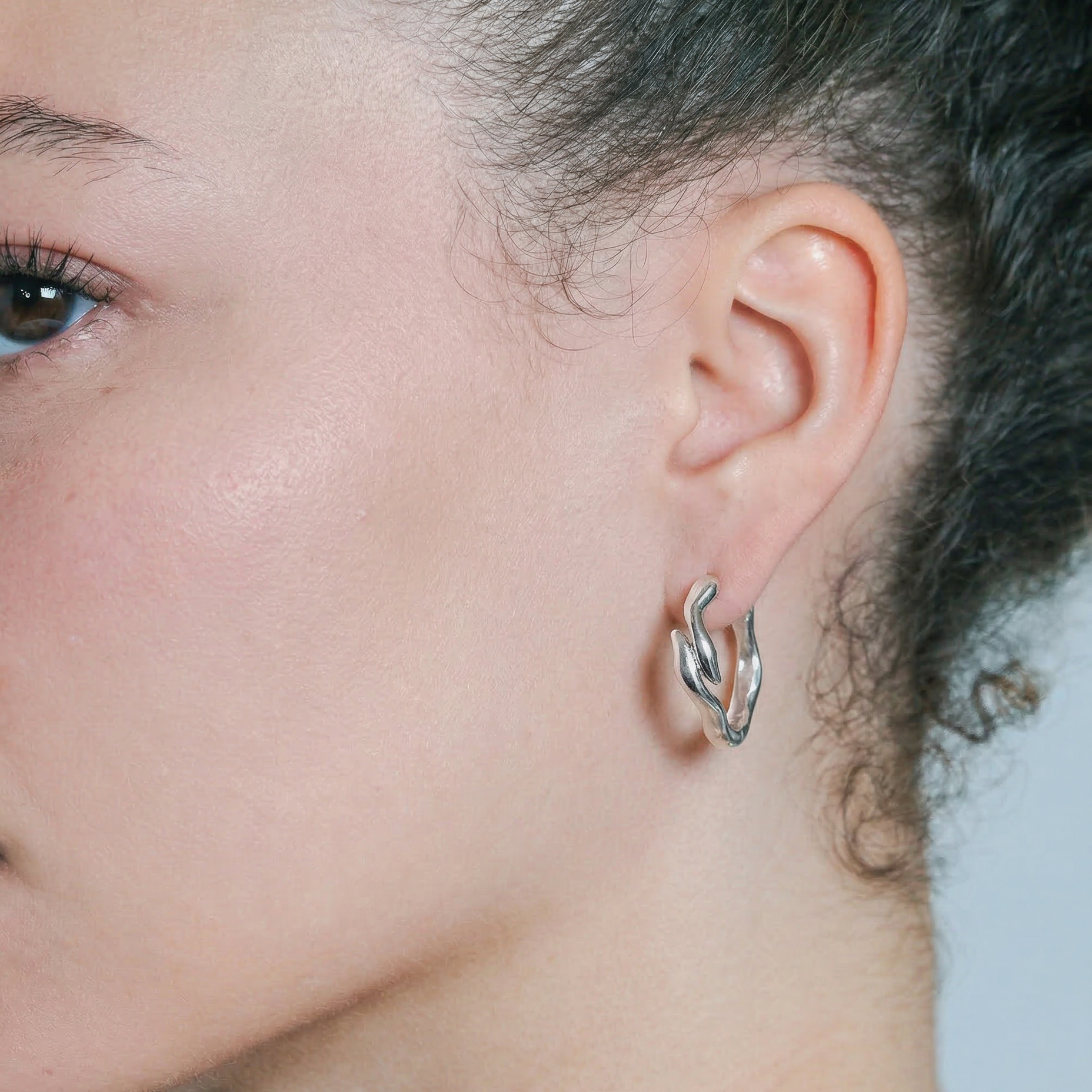 Close-up of a person wearing a silver hoop earring with a blurred background