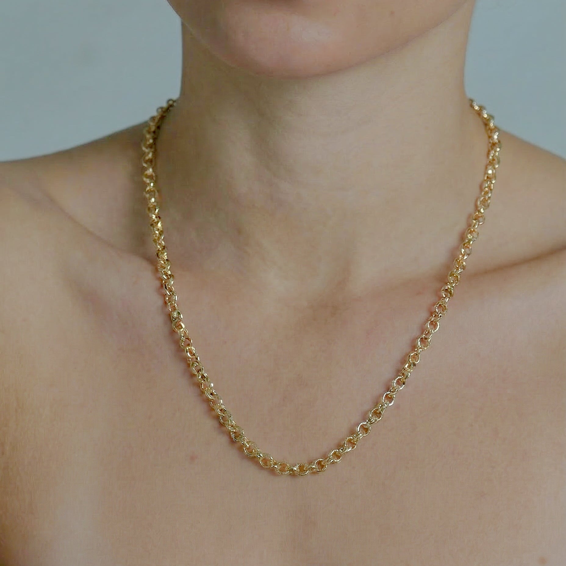 Gold chain necklace on a person with a neutral background
