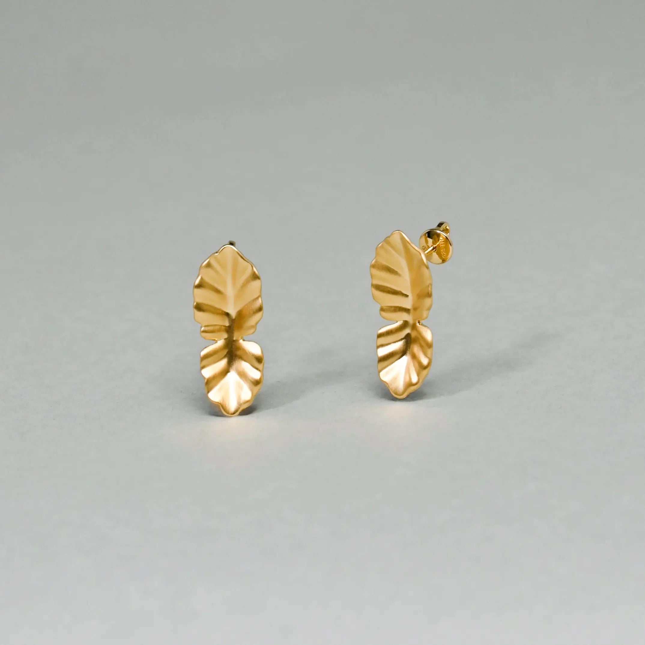 Pair of gold leaf-shaped earrings on a gray background