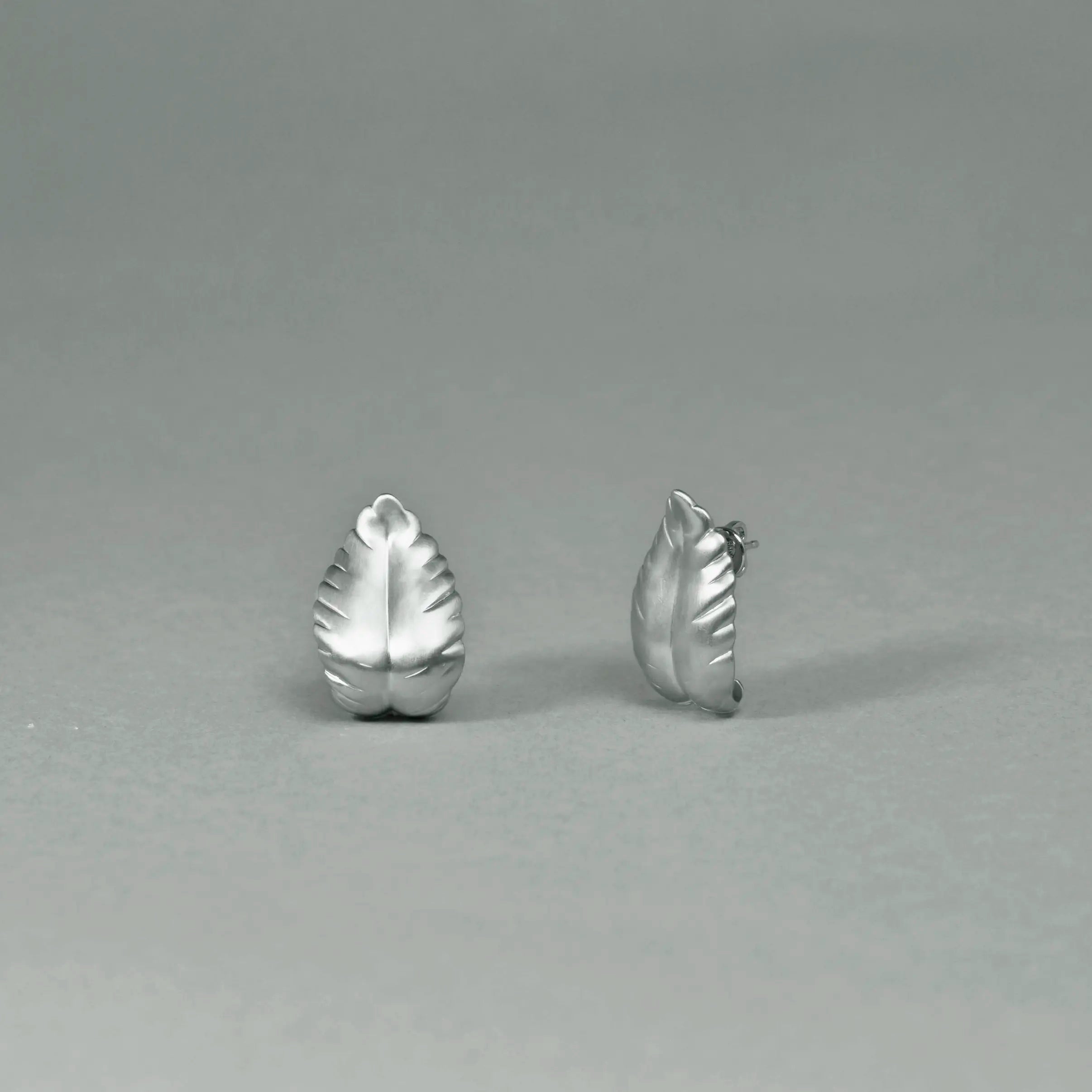 Pair of silver leaf-shaped earrings on a gray background
