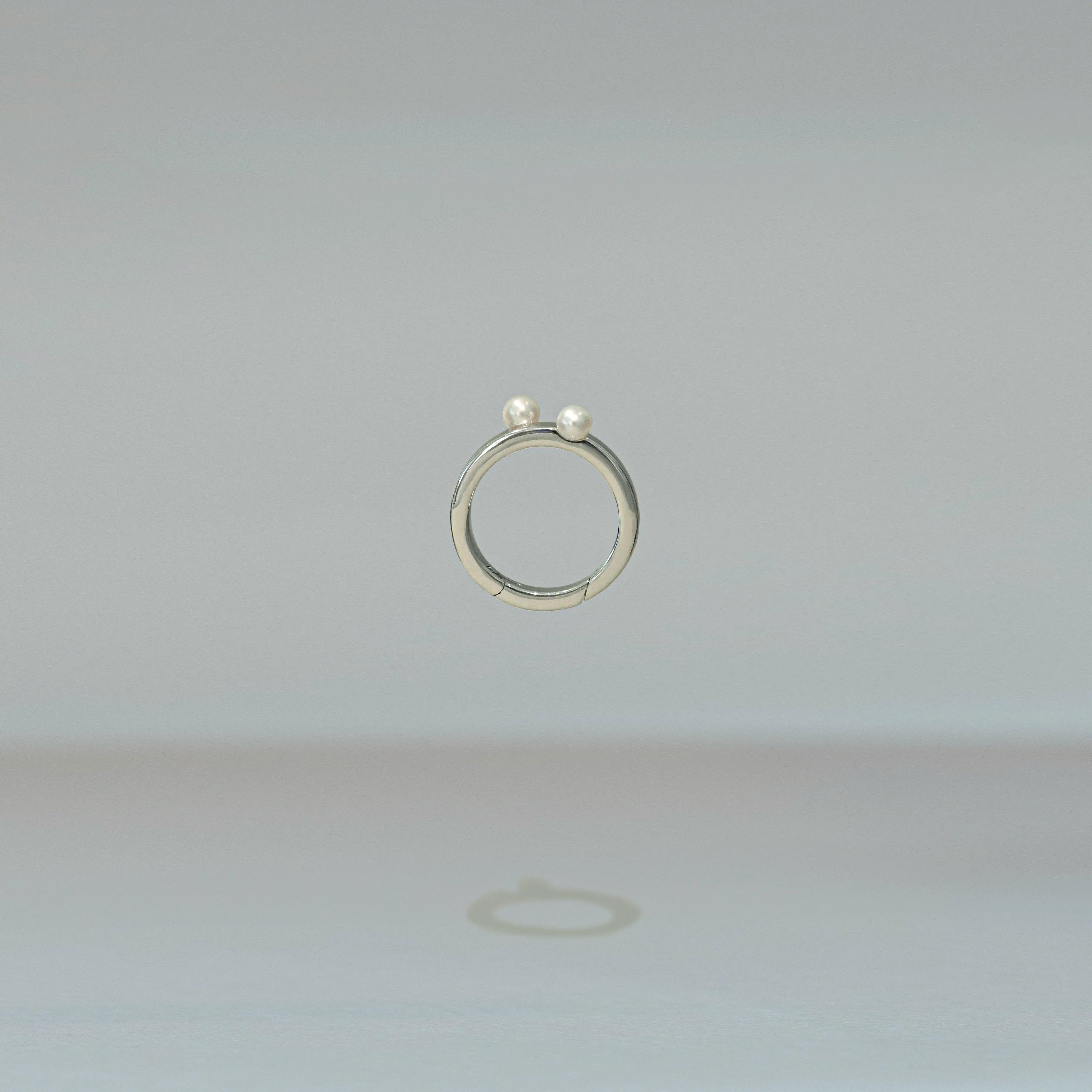 Silver ring with two small pearls on a light gray background