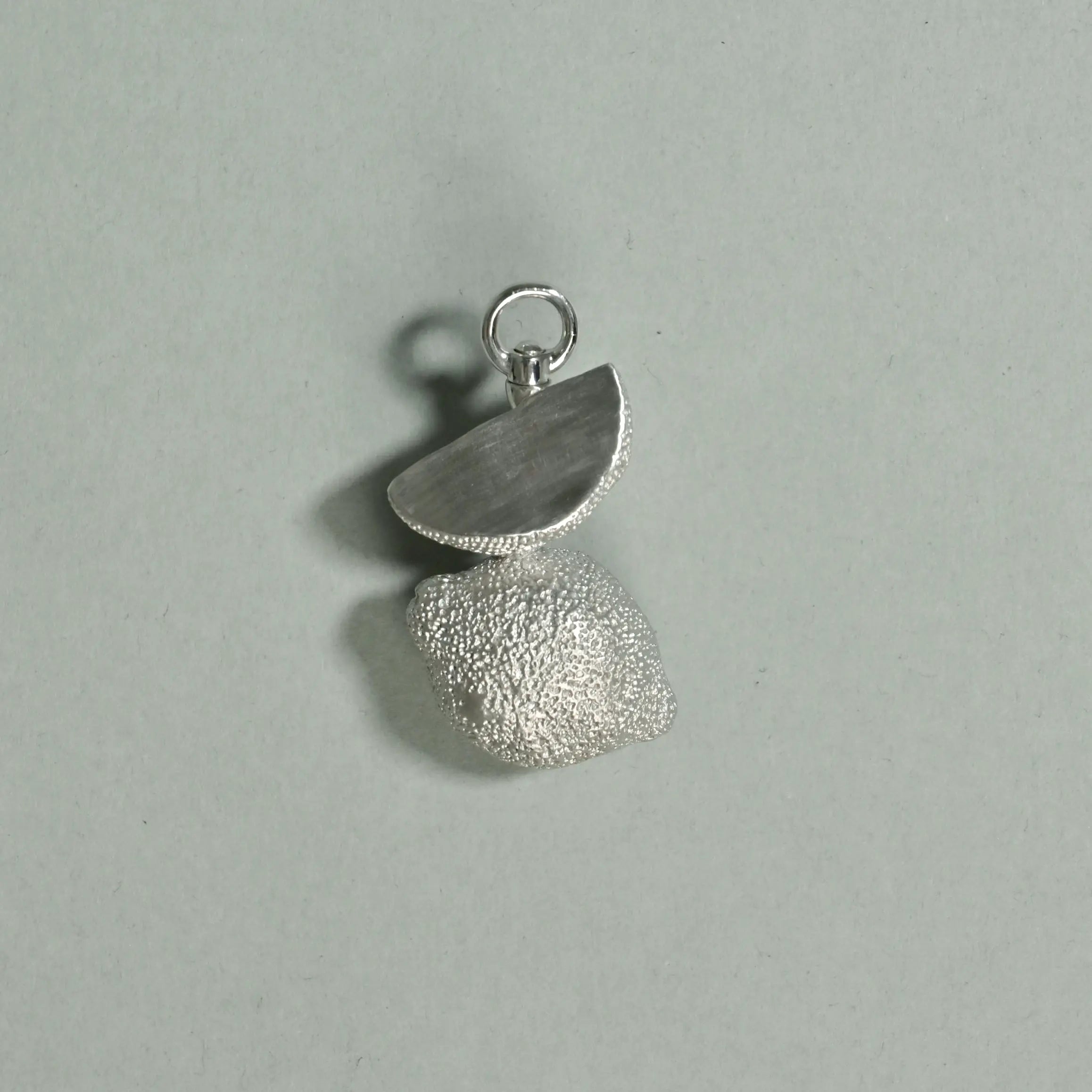 Silver pendant with textured surface on a light gray background