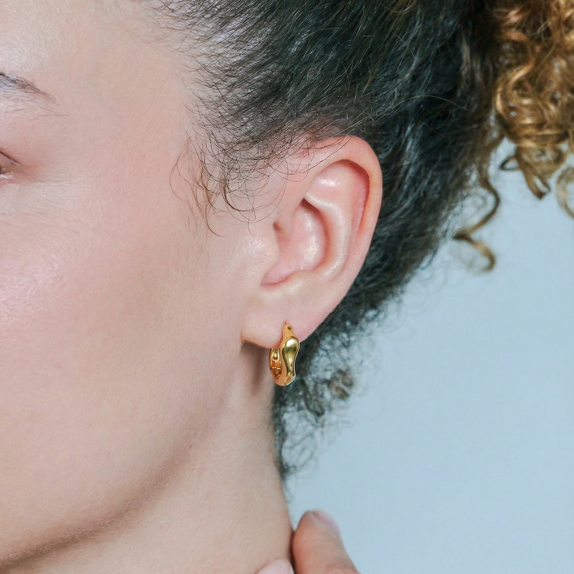 Close-up of a person wearing a gold hoop earring with a blurred background