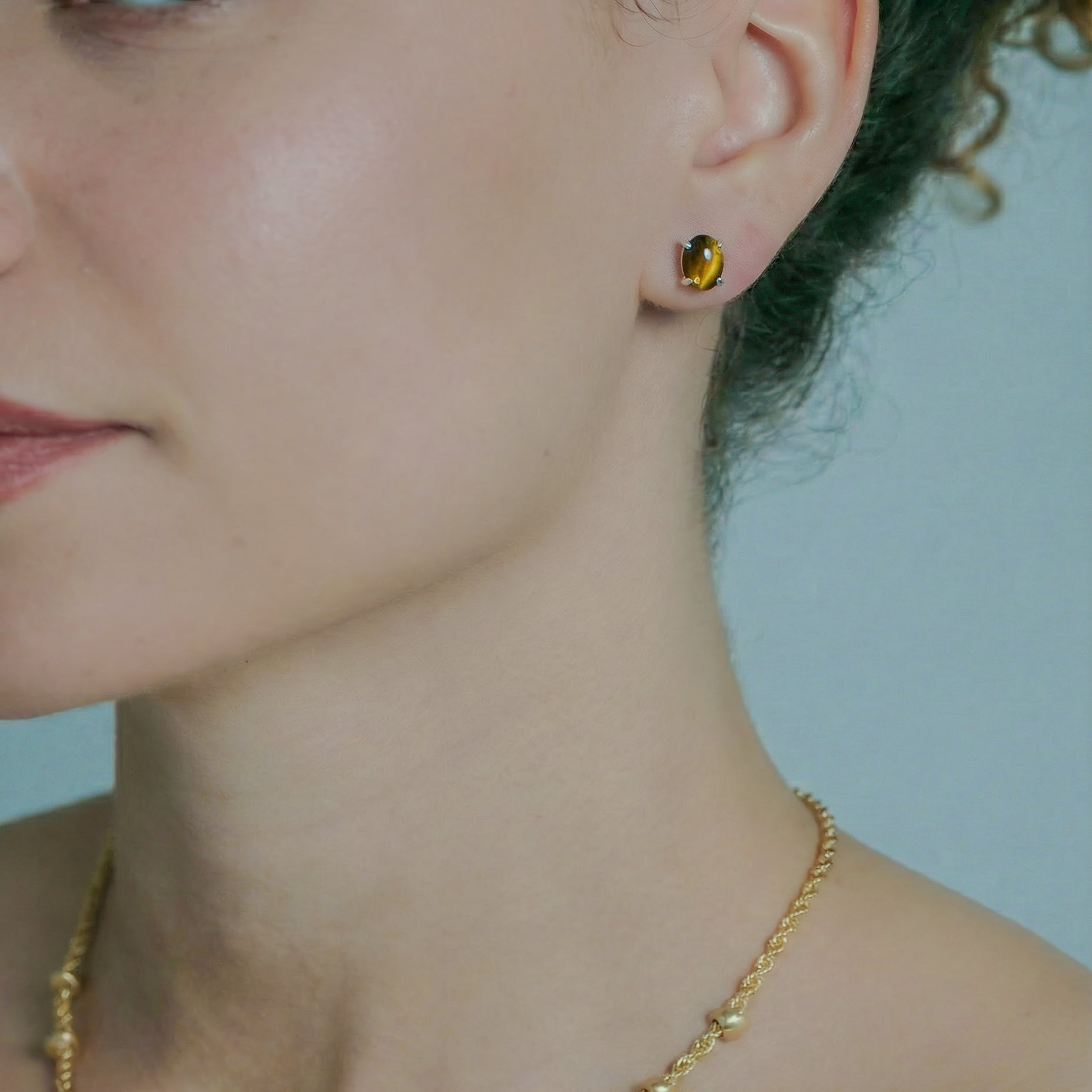 Close-up of a person wearing a gold necklace and amber earring against a light blue background